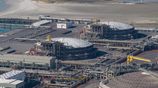 Aerial view of Fluxys LNG Terminal Zeebrugge featuring large circular storage tanks and complex industrial piping systems near the coast in Brugge, Vlaanderen, Belgium.