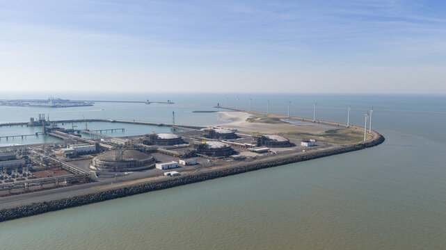 Aerial view of the Fluxys LNG Terminal Zeebrugge featuring large storage tanks, industrial infrastructure, and a row of wind turbines along the coastline in Brugge, Vlaanderen, Belgium.
