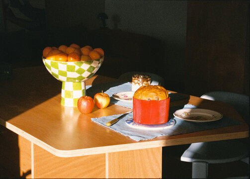 Analog close-up of a dining table eaturing a fruit bowl and small cake