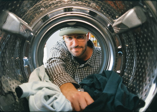 Analog-style shot from inside a clothes dryer of man removing laundry