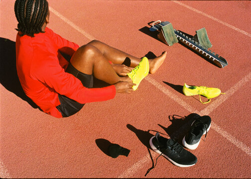 Film shot of athlete seated on running track tying his running shoes