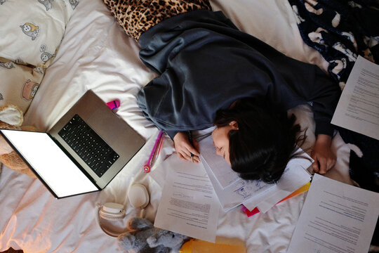 Exhausted student sleeping on study materials in bed