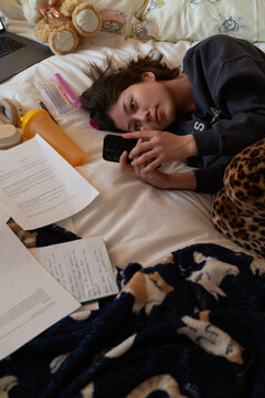 Student procrastinating on bed, using smartphone while studying