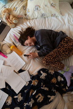 Person procrastinating studying on bed using phone