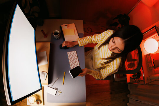 Woman using phone and computer at home office night