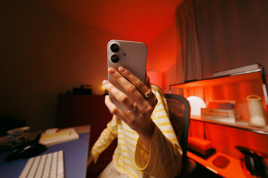Woman holding phone at home office desk at night
