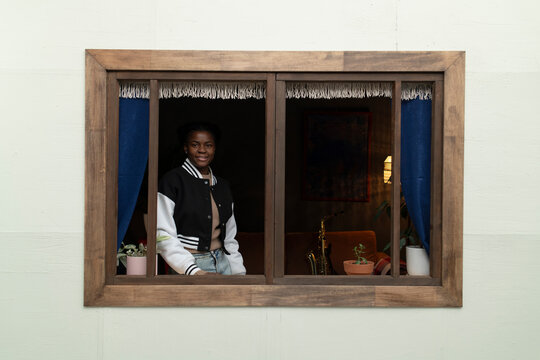 Young woman looking at camera from her home, view from outside