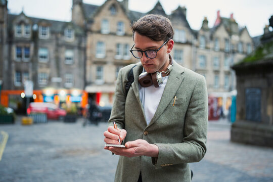 Man writing notes in city square
