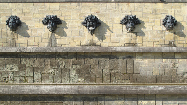Five Bronze Grotesque Mascaron Face Fountain Spouts on a Classic French Ch&acirc;teau Stone Wall in Sunlight