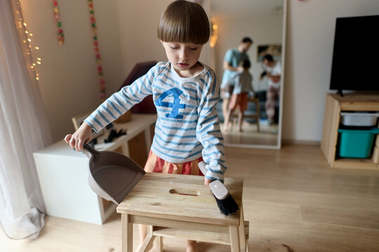 Little boy sweeping hair clippings with dustpan