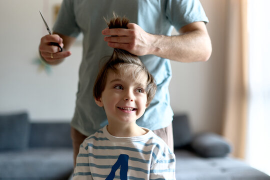 Smiling boy getting haircut from father at home