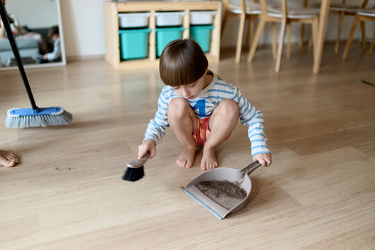 Little boy sweeping hair clippings with dustpan