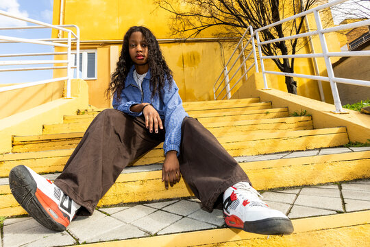 Girl in urban outfit looking at camera over yellow wall. Wide angle