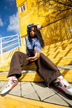 woman in urban outfit looking at camera over yellow wall. Wide angle