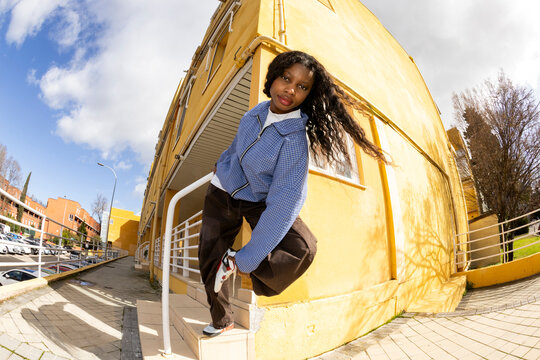 woman in urban outfit looking at camera over yellow wall. Fisheye