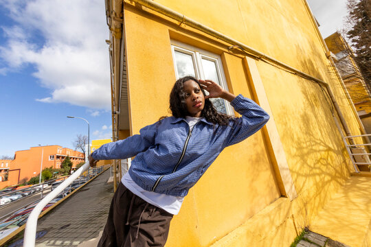 Portrait of woman in urban outfit looking at camera over yellow wall