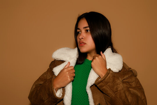 Woman in Brown Jacket Posing Against Plain Background