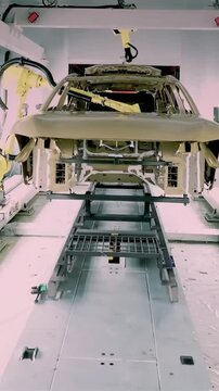 Vertical shot of yellow industrial robotic arms working on a vehicle chassis along an automated production line in a high tech Chinese car manufacturing plant.