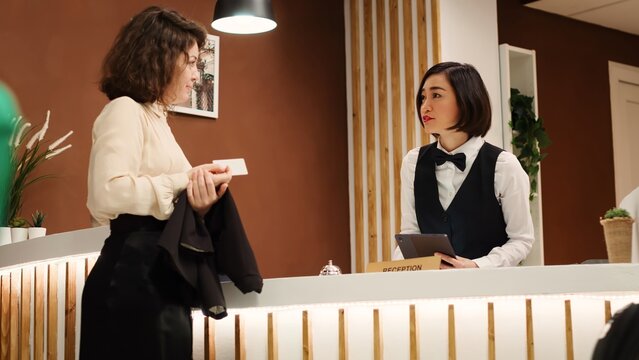 Hotel guest writing signature on tablet and being handed room card key by asian receptionist during check in process. Teamworking concierge staff helping tourist in resort lounge