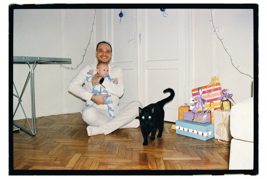 Smiling man holds baby sitting with gifts and cat
