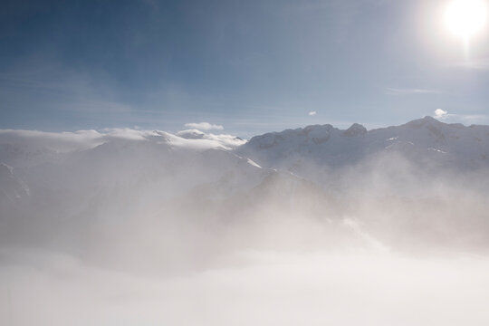 Sunlit Fog Engulfing Snow-Covered Mountain Peaks