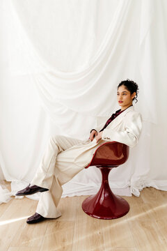 Woman posing in tailored beige suit and maroon chair