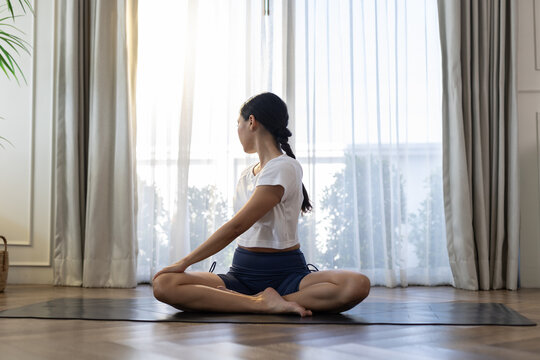 woman practicing seated spinal twist yoga pose indoors near window. Flexibility training, home workout, healthy lifestyle, wellness, balance, mindfulness, yoga relaxation and body mobility concept