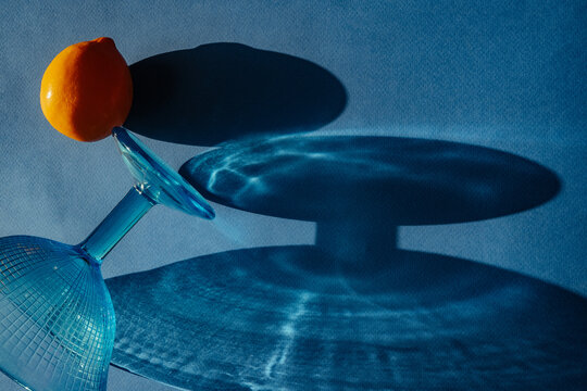Shadows and shapes from a glass and orange on a blue surface