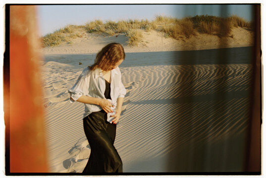 Woman walking across sunlit sand dunes