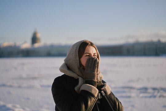 Young Woman In Winter Coat And Hood Warming Hands Outdoors 