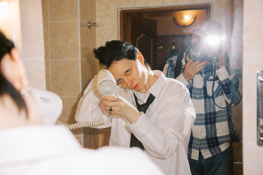 Person Uses Hair Dryer in Bathroom While Someone Takes Picture