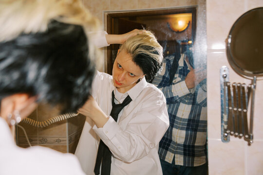 Person Styles Hair in Bathroom While Looking in Mirror With a Tie