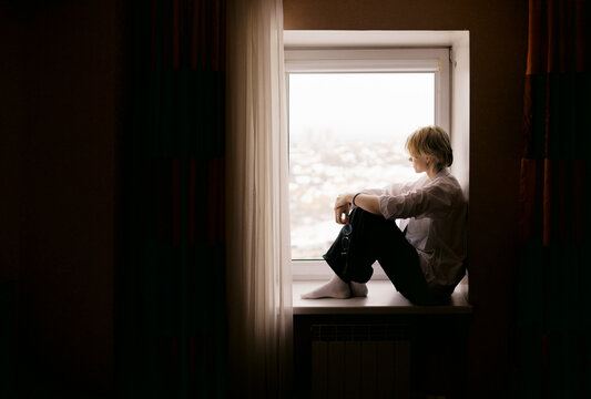 Woman Sits by Window and Looks Outside at City View