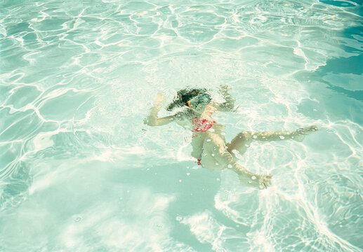 Child swimming and diving underwater in a clear pool
