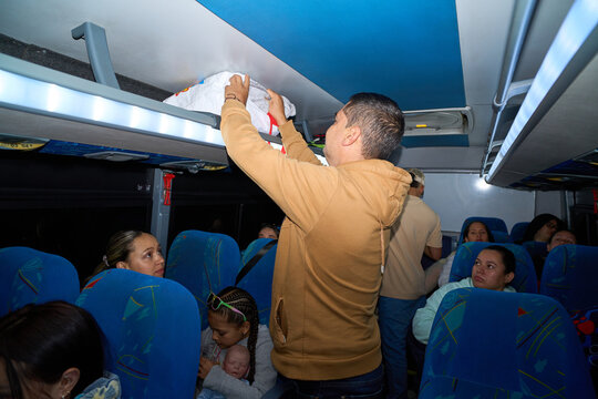 Man placing luggage on bus overhead rack, traveling with passengers
