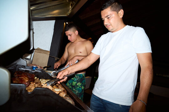 Two men grilling meat outdoors at a night bbq party