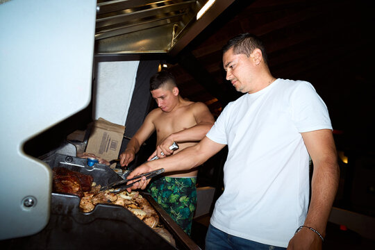 Men grilling meat at a night barbecue social gathering