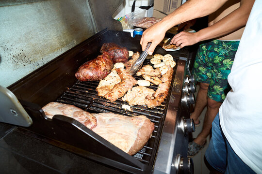 Friends grilling barbecue meat on outdoor gas grill