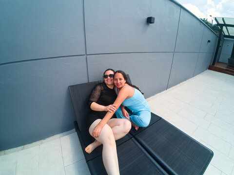 Women friends embracing on sun lounger relaxing outdoors