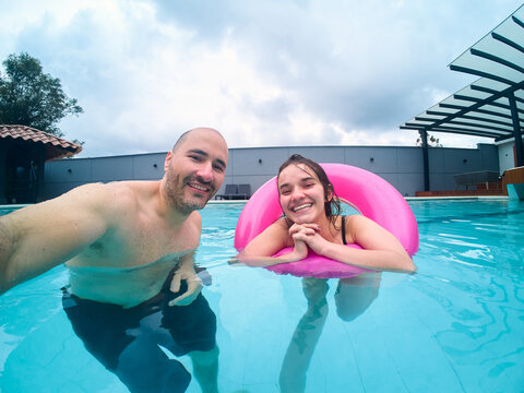 Happy couple friends taking selfie in swimming pool