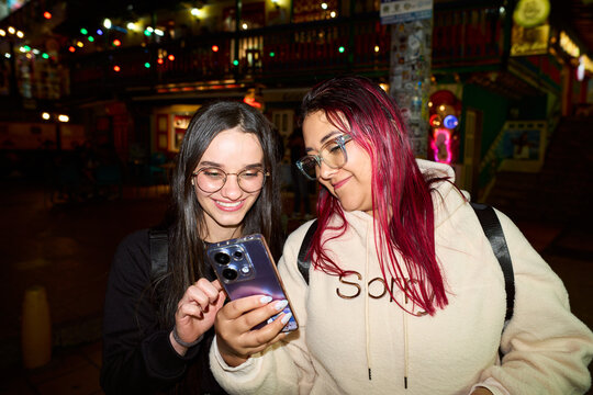 Women friends enjoying smartphone content on city street