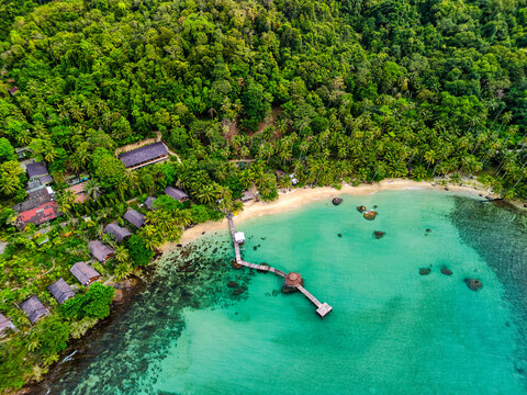Aerial view of a tropical beach resort with wooden bungalows and a long pier over turquoise water in Ko Kut District, Trat, Thailand.
