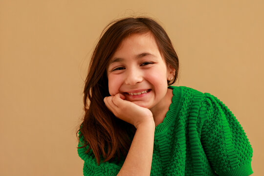 Young Girl Smiles While Resting Her Chin on Her Hand Indoors