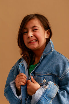 Girl Smiles and Winks in Denim Jacket Against Plain Background
