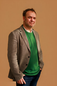 Man in a Blazer and Sweater Poses Against a Plain Backdrop