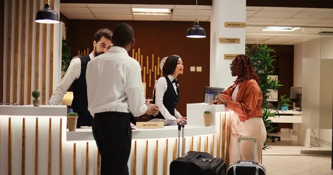 Friendly smiling concierge personnel assisting tourists with room registration. Cheerful front desk receptionists answering customer inquiries about hotel amenities during guests check in process