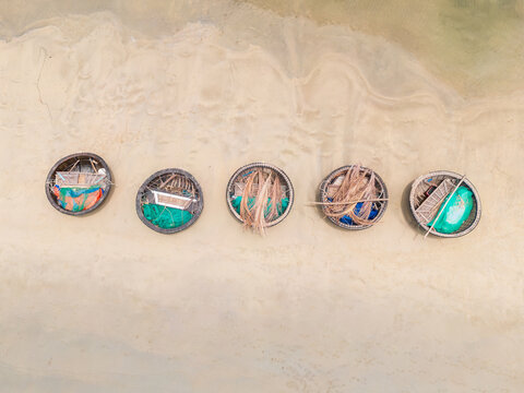 Five Vietnamese basket boats lined up on a flat sandy beach