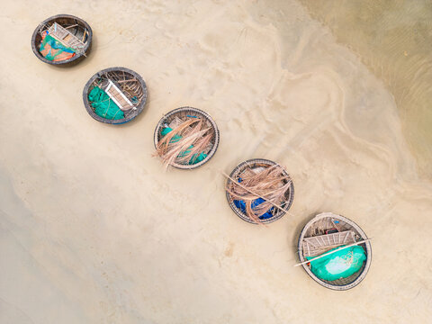 Five Vietnamese basket boats lined up on a flat sandy beach