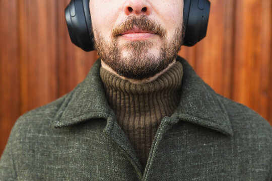 Close up of bearded man wearing olive green wool coat and headphones.