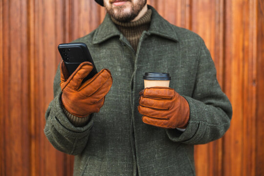 Man in stylish winter coat and leather gloves using smartphone